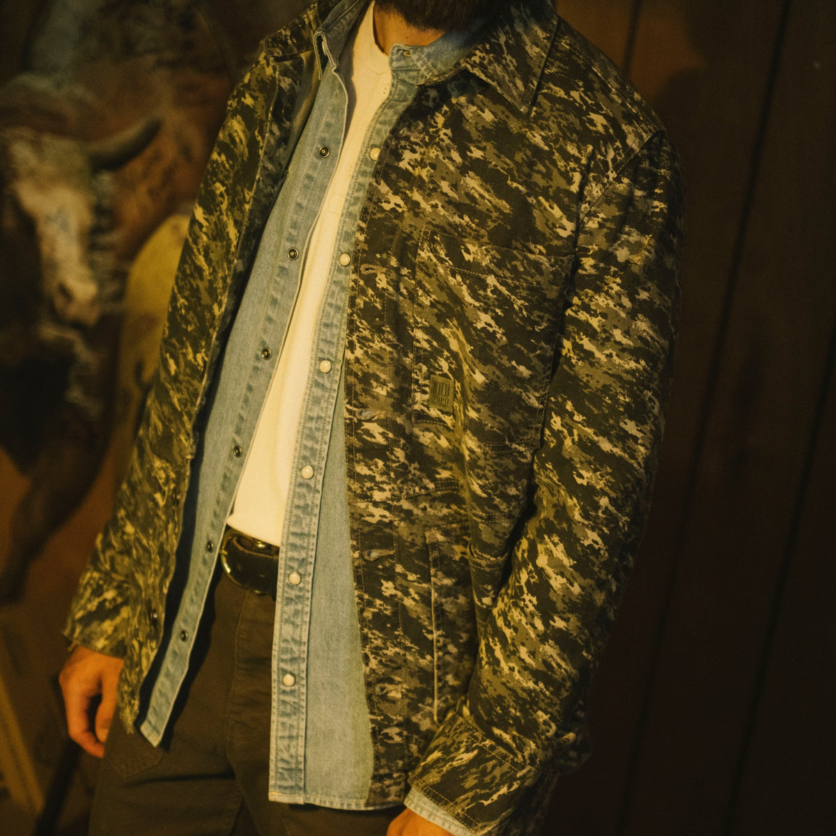 Person wearing a camouflage jacket over a denim shirt with a blurred background